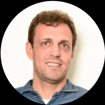 Smiling man with short brown hair and light eyes wearing a blue denim shirt.