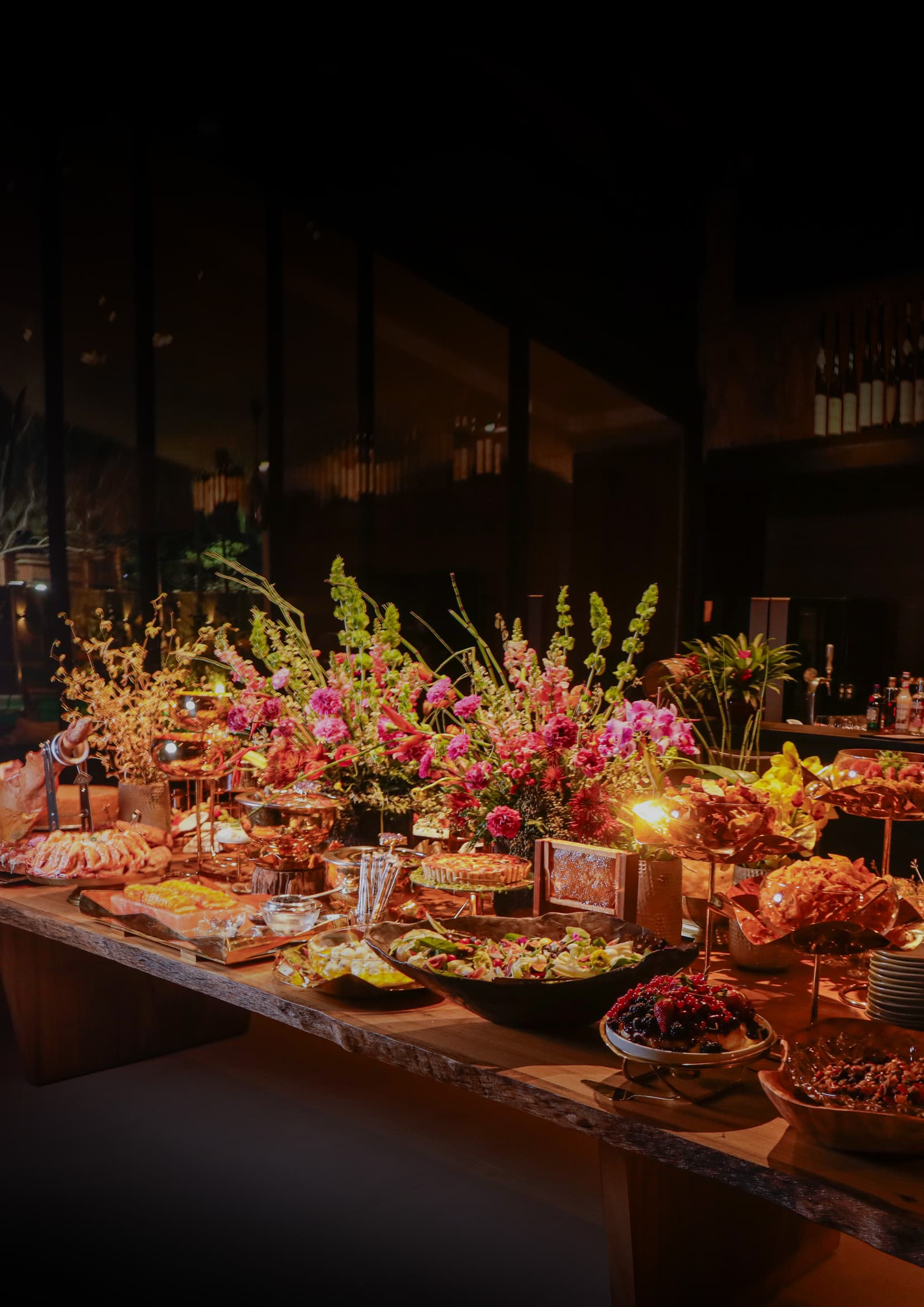 Lavish buffet table featuring gourmet appetizers, salads, and large, vibrant pink floral centerpieces.